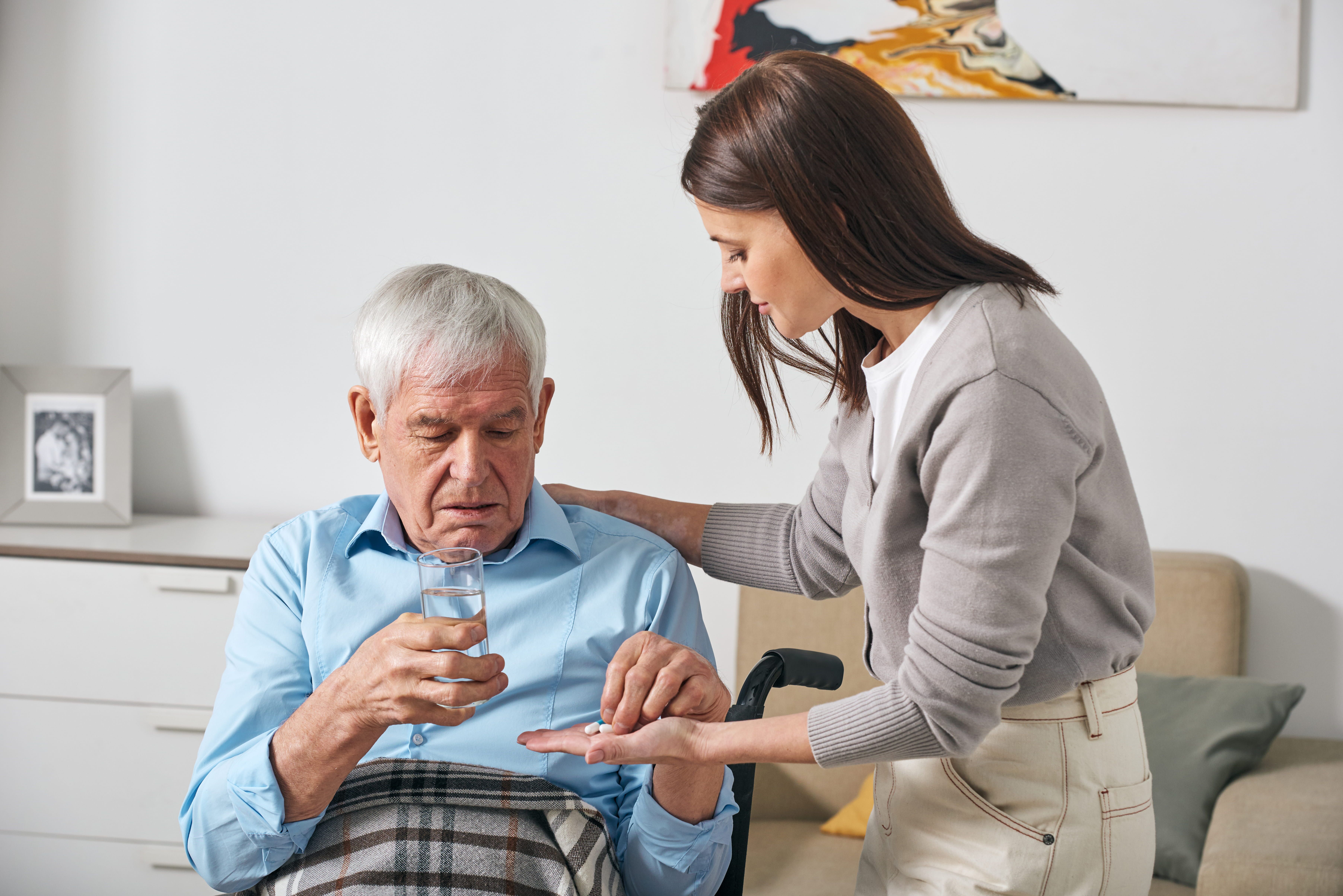 young adult daughter giving pills senior father while taking care him after stroke  1 